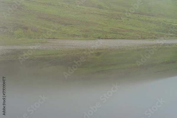 Fototapeta Misty Morning Reflection on a Calm Lake in a Green Valley