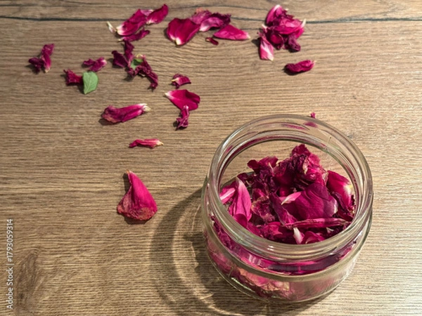 Fototapeta Elegant background with fresh and dried rose petals in a glass jar and scattered on a wooden surface under soft light. Floral design for wellness, beauty themes. Aromatic ingredient for cosmetics.