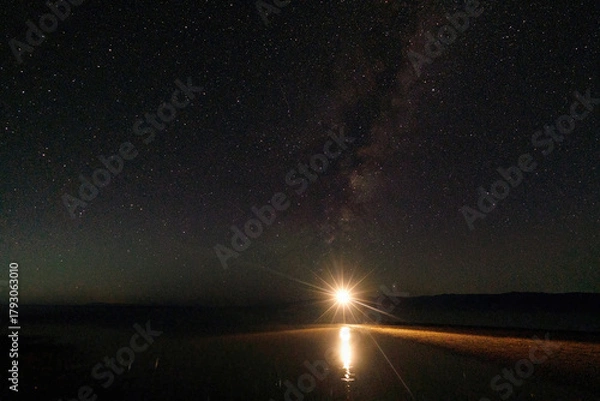 Fototapeta A starry night over the water surface, bright light illuminates the path to the Milky Way. The serenity and grandeur of nature in one shot