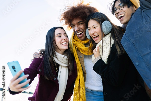 Obraz Diverse group of teenage friends having fun taking selfie portrait at city street on winter. Holiday lifestyle and technology concept