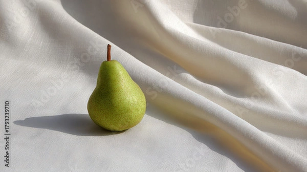 Fototapeta fresh ripe pear rests elegantly against backdrop of soft linen fabric illuminated by ultrabright sunlight