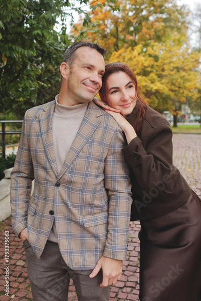 Obraz Happy smiling couple embracing and leaning heads together, showing affection on a brick path surrounded by autumn trees