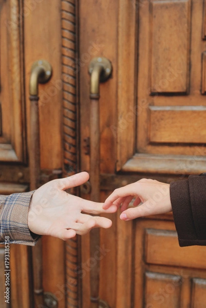 Obraz Close-up of a couple's hands reaching out to touch, symbolizing connection and affection against a massive old wooden door