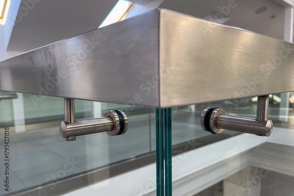 Fototapeta Close-up of a modern stainless steel railing corner on a glass balustrade, emphasizing seamless metalwork, contemporary design, and polished architectural details for commercial and luxury interiors.