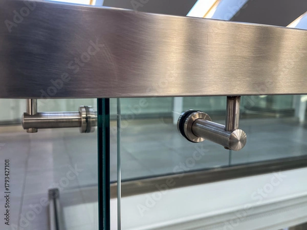 Fototapeta Close-up of a modern stainless steel railing corner on a glass balustrade, emphasizing seamless metalwork, contemporary design, and polished architectural details for commercial and luxury interiors.