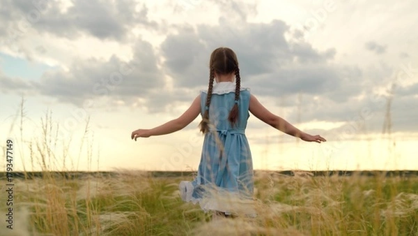Fototapeta Baby girl playing superhero in nature. kid girl run in park. Happy little girl in dress running with raised hands on grass meadow. Children's dreams. Cheerful little girl play running in summer park