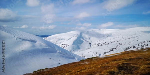 Fototapeta Panoramic view of snowy mountain slopes and deep valley under clear blue sky in bright sunlight. Peaceful winter nature background.