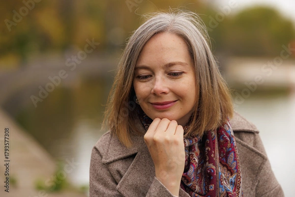 Fototapeta Woman reflecting by the serene waters of a tranquil park in autumn