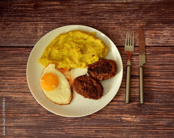 Fototapeta Fried egg, mashed potatoes and two meat patties in a round plate on a wooden table.