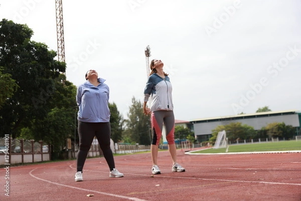 Obraz Two slim and plus size woman with sport jacket together stretch warm-up exercise on an outdoor running track, wellness and healthy lifestyle