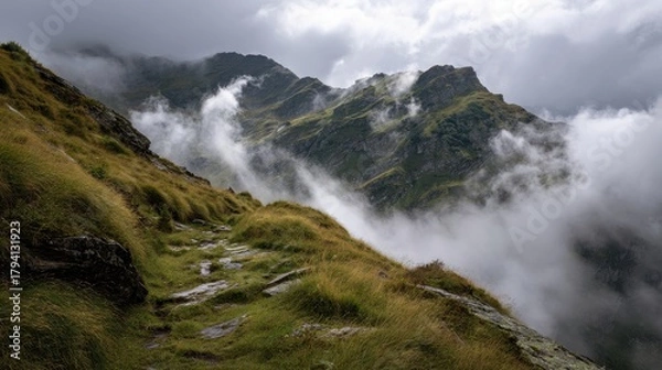 Fototapeta Winding stone path along a grassy mountain ridge enveloped in dramatic clouds and mist.