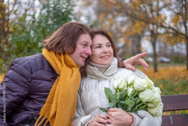 Fototapeta Midlife couple enjoying a romantic moment in autumn park, surrounded by colorful leaves, holding roses, sharing laughter and warmth, celebrating love and connection
