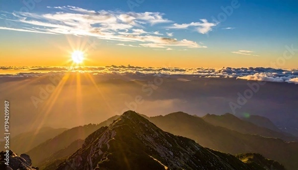 Fototapeta A scenic sunrise over a mountain range, with sunlight piercing through the clouds and illuminating the peaks