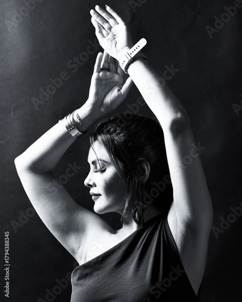 Fototapeta Monochrome portrait of an elegant woman captured in graceful motion with raised arms. Fine-art style lighting highlights emotion, beauty, and artistic expression. Perfect for fashion and conceptual