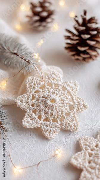Fototapeta Handmade crocheted snowflake ornament on warm cream background with pinecones and fairy lights in cozy Scandinavian holiday flatlay