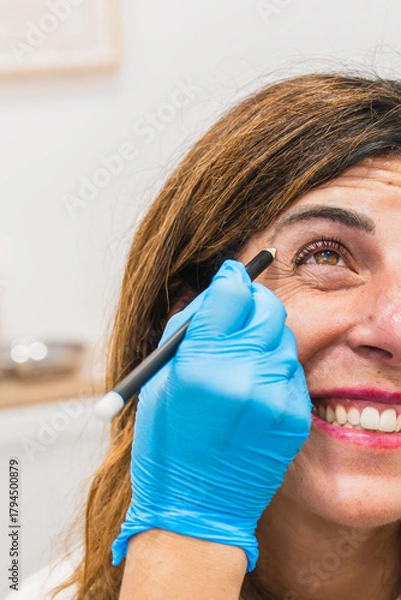 Fototapeta Professional drawing lines on mature woman's face, preparing for cosmetic injections to reduce wrinkles around her eye