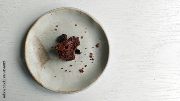 Fototapeta Remains of some chocolate chip cookies on small plate. Handmade rustic ceramic saucer with crumbs set against light wooden background. Breakfast is over on wooden table