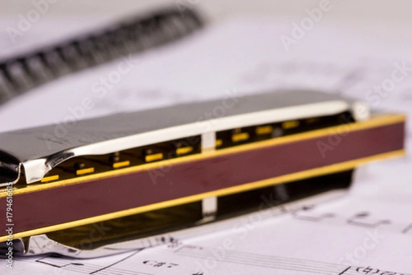 Fototapeta A metal harmonica on an open music book. taken in close-up, with space for text, an object, or an advertisement