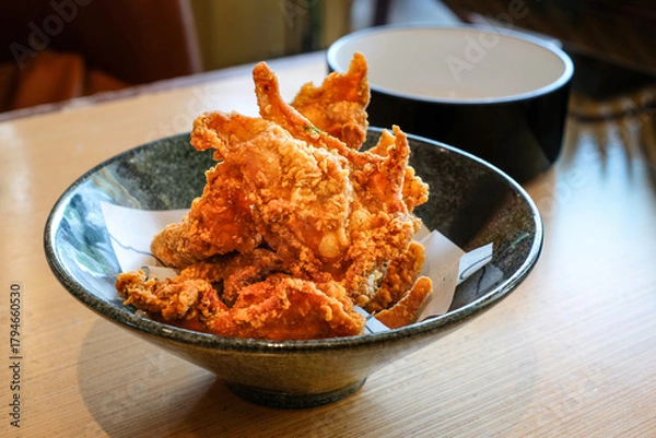 Obraz Crispy fried chicken skin served on a black ceramic bowl over a wooden table under natural light. Perfect for restaurant menus, snack product ads, or food blog illustrations