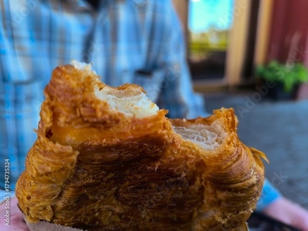Fototapeta A young man holds a fresh croissant in his hand. Selective focus on his hands against a blurred background.
