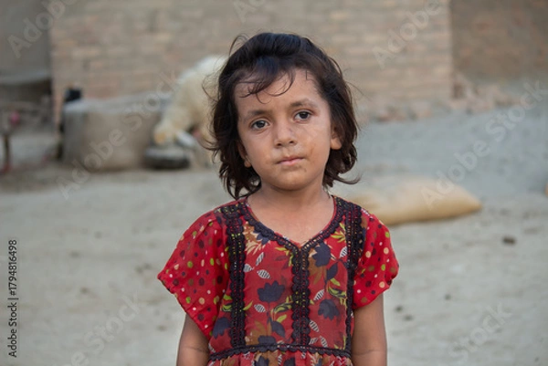 Fototapeta Rural village girl standing outdoors in traditional colorful dress, natural light portrait with calm and innocent expression