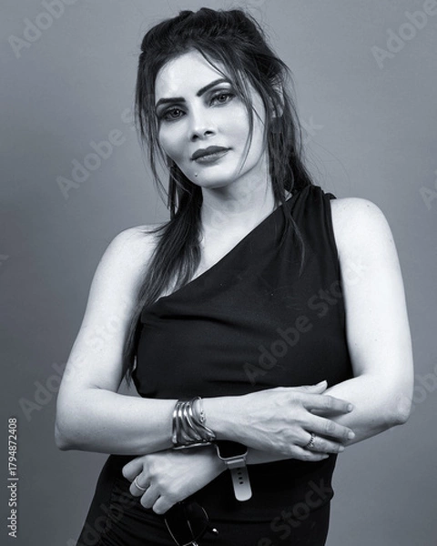 Obraz Monochrome studio portrait of an elegant woman wearing a black dress. A confident and modern fashion image symbolizing timeless style and grace.