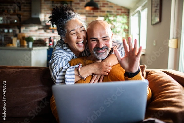 Fototapeta Happy senior couple hugging and waving on video call at home