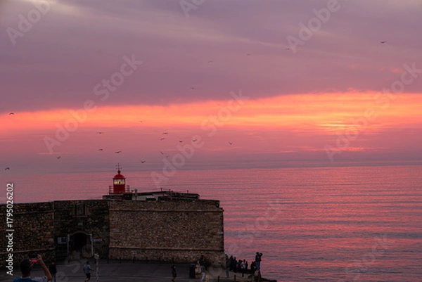 Obraz Scenic sunset over the Atlantic Ocean with iconic red lighthouse at Forte de Sao Miguel Arcanjo in Nazare, Portugal