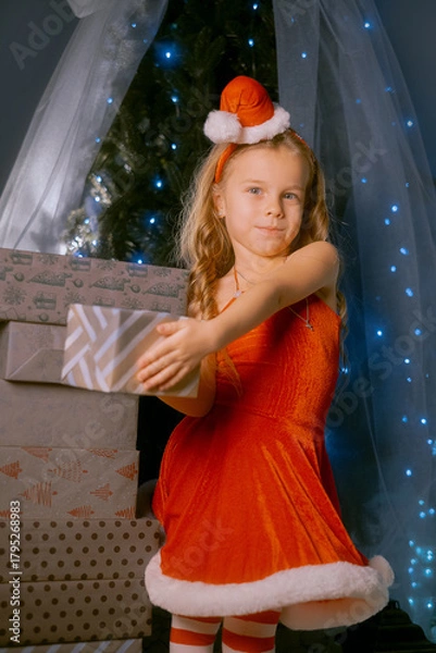 Fototapeta Elegant young woman dressed as Santa Claus enjoying the festive season next to a decorated Christmas tree.