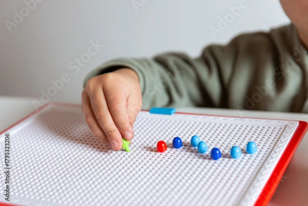 Fototapeta Child inserting colored pegs into mosaic board. Concept of creativity development, focus, and fine motor skill learning during early childhood education process.
