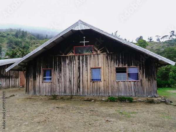 Fototapeta A rustic wooden church standing in a remote mountain village, featuring weathered timber walls, a cross on the roof, and a serene natural backdrop. Perfect for themes of faith, tradition, and rural li