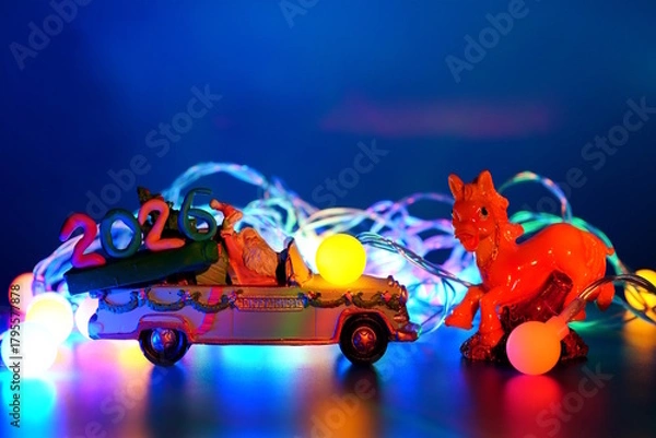 Fototapeta A toy car with Santa Claus and the date 2026. There is a glowing Christmas tree garland and a horse figurine nearby.