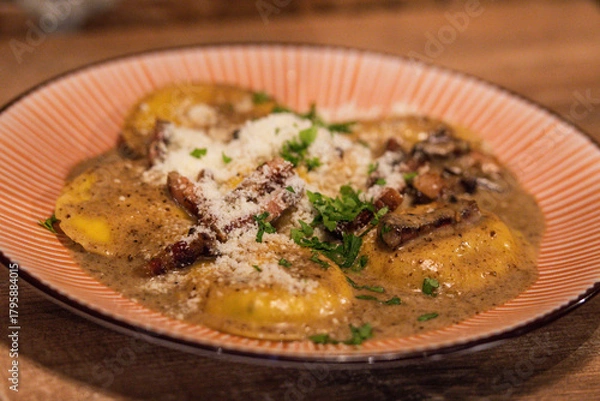 Fototapeta Homemade ravioli with porcini mushrooms and crispy guanciale, served in a creamy sauce and garnished with parsley and parmesan cheese 