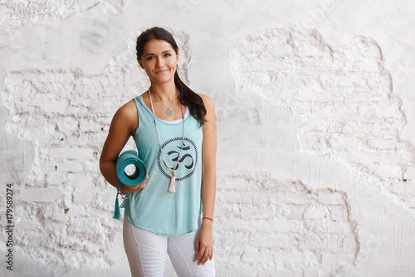 Obraz Portrait of attractive woman holding green yoga or fitness mat after working out at home or in club. Friendly smiling sport instructor looking at camera. Healthy life concept