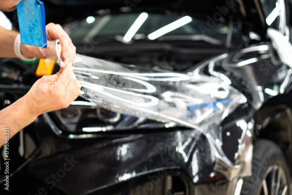 Obraz A car wrapping specialist applies a polyurethane film to the car. Selective focus. PPF protective film against chips and scratches. Car wrapping, detailing, tuning and styling. Detailer smoothes PPF. 