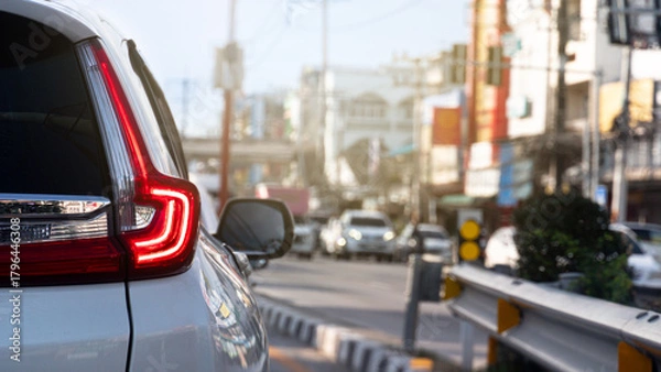 Fototapeta Rear side of luxury white car with trun on brake light. Stop on the junction from traffic light control. Opposite raod with many cars queue up. Blurred of town at day time.
