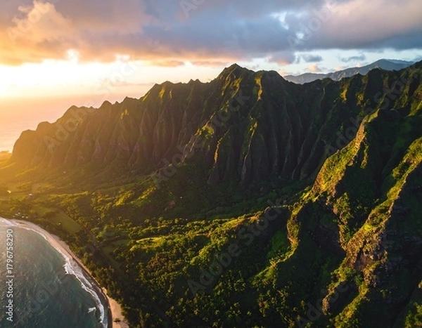 Fototapeta A vibrant sunset casts golden light on rugged mountains bordering a serene beach. The sky is filled with colorful clouds