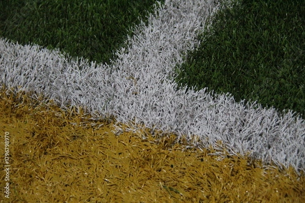 Fototapeta Close-up of colorful turf intersection with green, white, and yellow lines. Ideal for sports, field design, or athletic-themed visual content