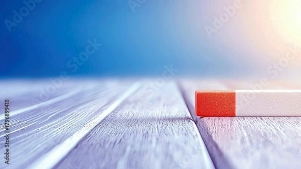 Fototapeta A close-up shot of a red and white rectangular object resting on a light-colored wooden surface, with a soft blue background.