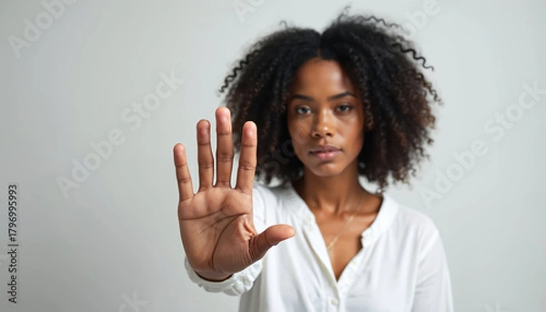 Fototapeta African American woman raises hand in stop gesture. Female shows hand in denial on white background. Black person protesting domestic violence. Fight against discrimination. Stop sign