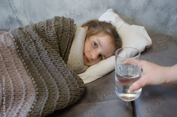 Obraz A little girl is lying in bed sick. A glass of water in bed