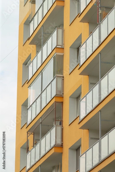 Fototapeta A close-up view of a contemporary yellow apartment building showcasing multiple balconies and glass railings, emphasizing modern architecture.