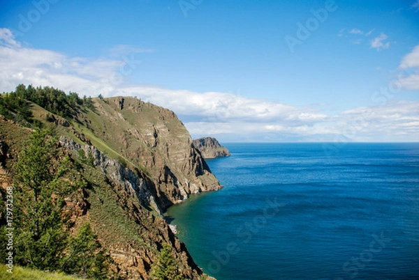 Fototapeta Blue sky with clouds over sea surface. Rocky coast view in sunny day