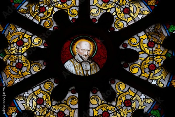 Fototapeta This stained glass window showcases Saint Vincent de Paul, surrounded by intricate floral designs. Located in the Basilica of Notre-Dame-de-Buglose, Landes department.