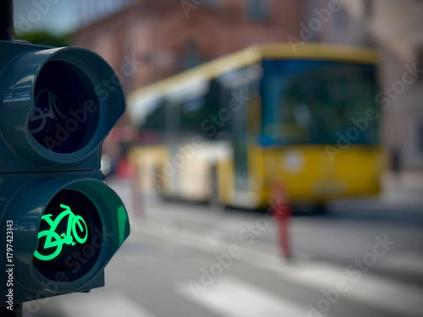 Fototapeta Closeup of bicycle traffic light showing illuminated green cycling symbol on urban street with blurred road background and bright daylight