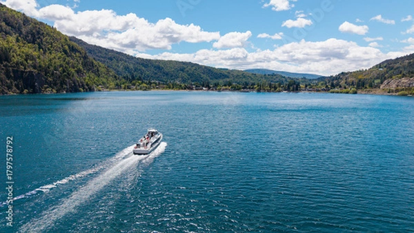 Fototapeta A tourist boat sails on Lake Lacar, with the city of San Martin de los Andes in the background.