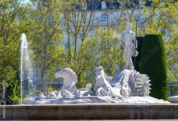 Obraz Close-up of Madrid’s Fuente de Neptuno, showing the white marble Neptune with trident, surrounded by horses and a strong water jet, all framed by vibrant green trees