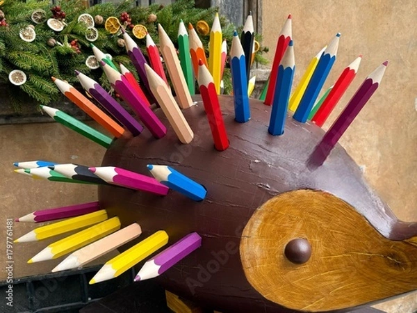 Fototapeta a colorful decorative sculpture resembling a hedgehog, with its spikes made from large, vibrant wooden pencils. The playful artwork has a brown body and a wooden face