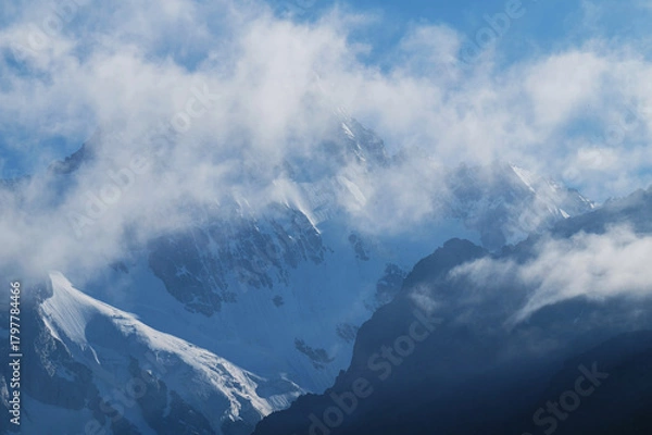 Fototapeta Silhouettes of snow-capped mountains and low clouds at dawn