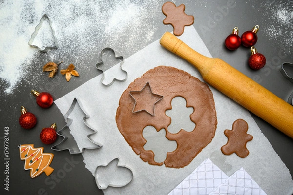 Fototapeta Top view of gingerbread cookie preparation with star, tree, and gingerbread man cutters beside a rolling pin and holiday ornaments. Great for Christmas promotions, seasonal digital content.